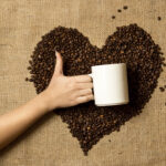 photo of woman holding mug against heart made of coffee beans